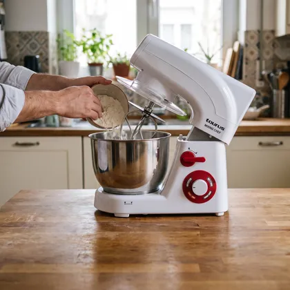 Mâini turnând făină în bolul unui mixer Taurus Mixing Chef, pe blatul de lemn al unei bucătării